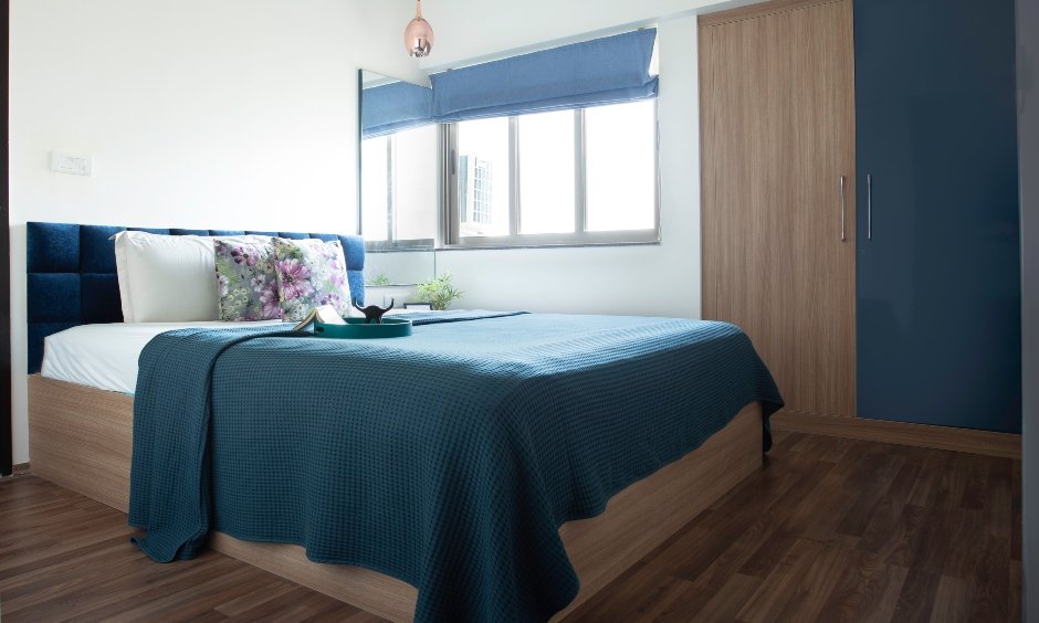 The master bedroom has a bed with a cushioned headboard and a wardrobe designed by best home interior designer in mumbai